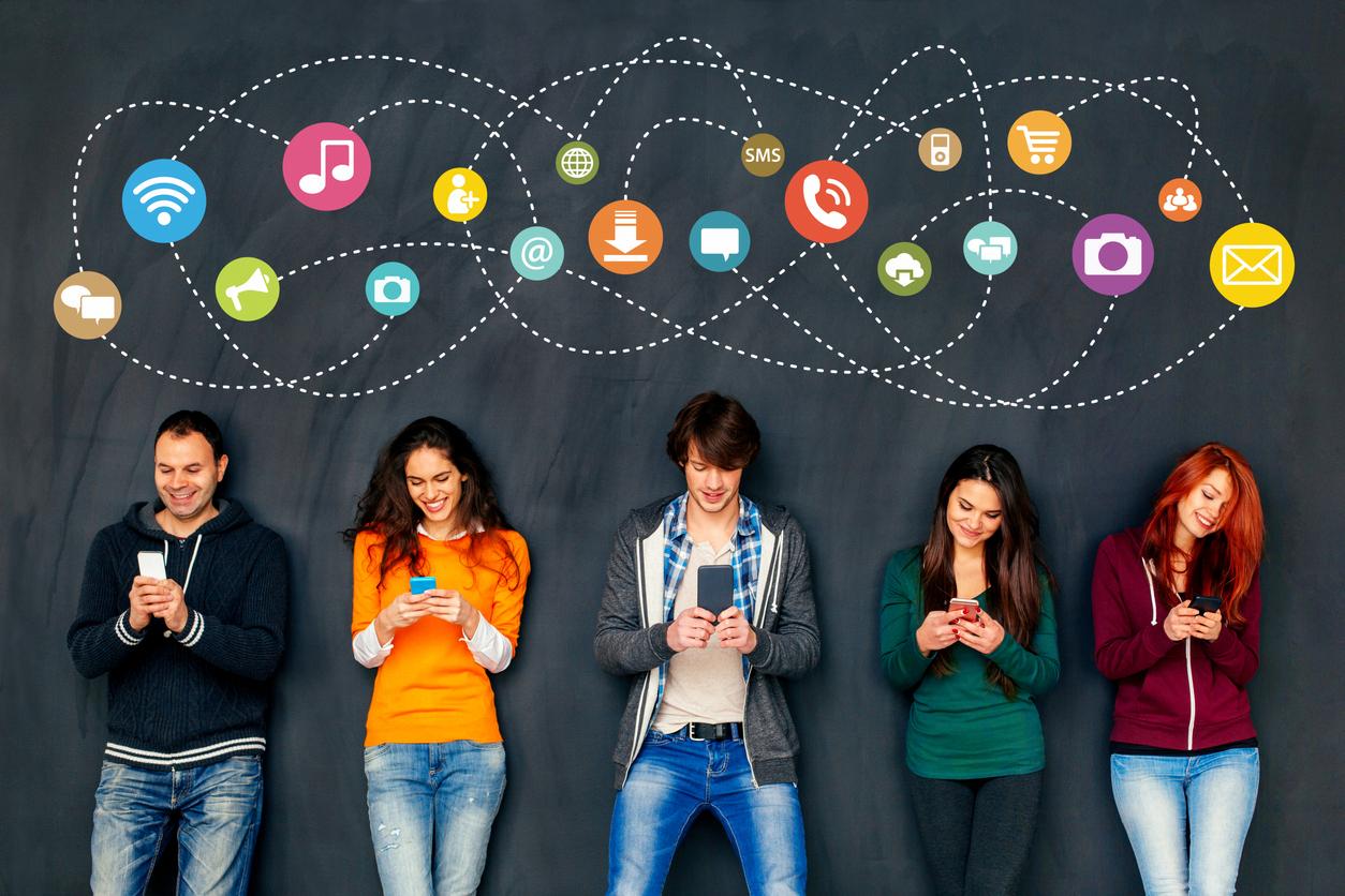 Smiling young people holding smart phones in front of big chalk blackboard